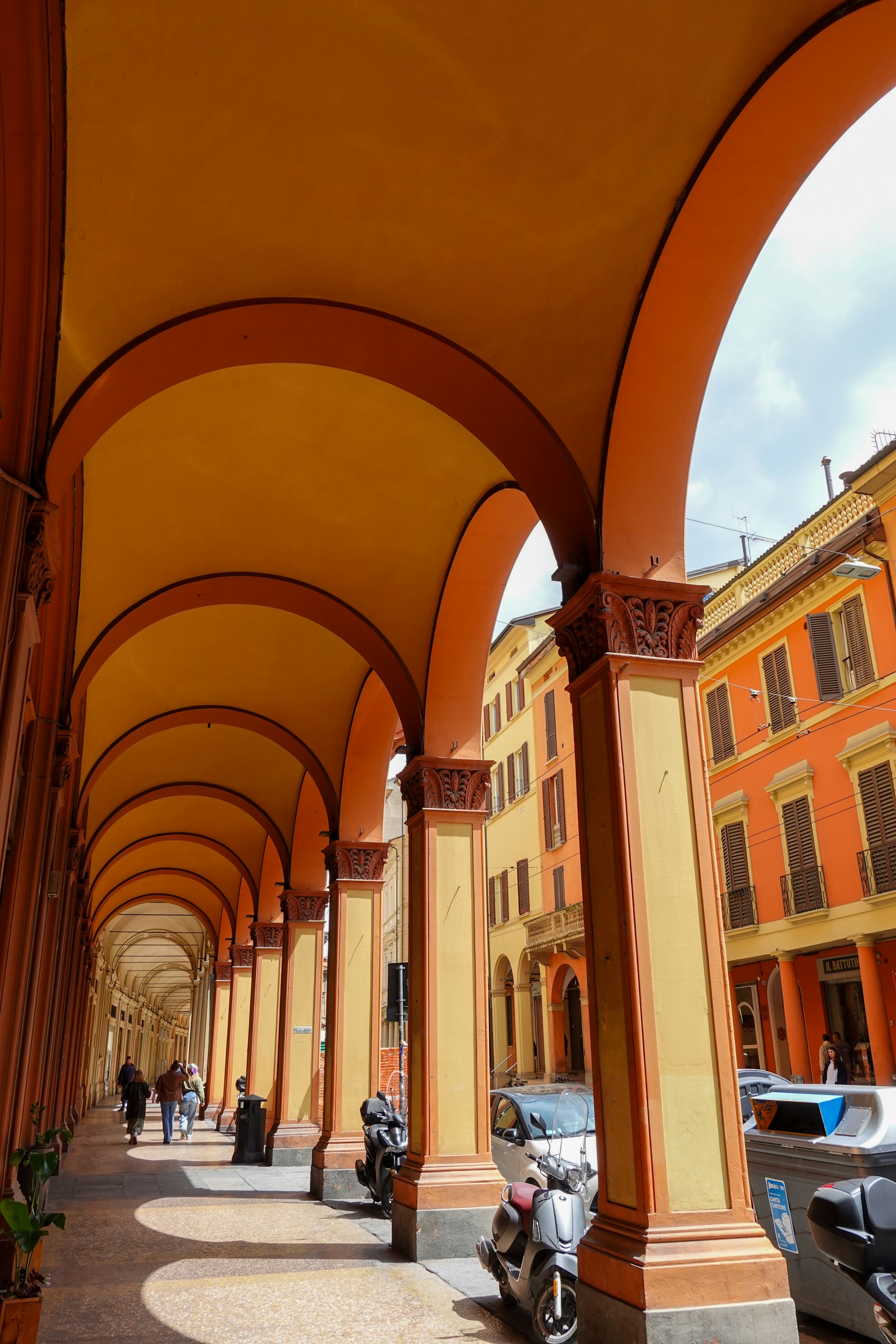 People walking beneath Bologna's warm-colored porticoes